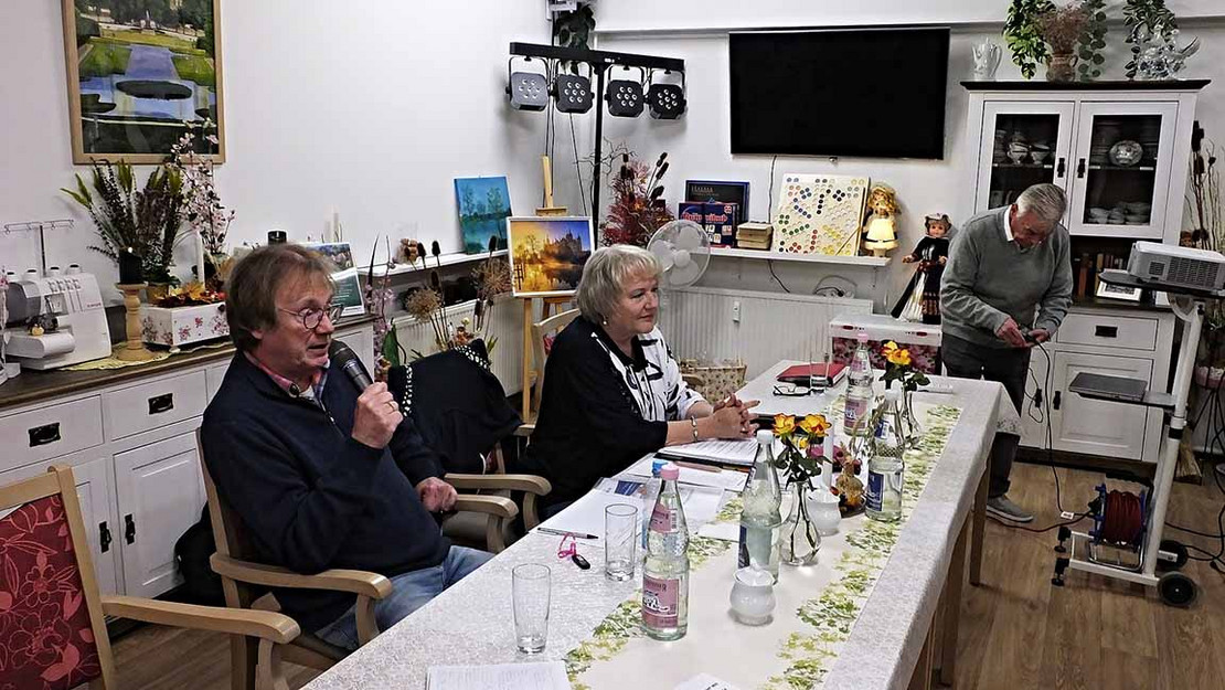 Drei Personen sitzen an einem Tisch, einer hält ein Mikrofon in der Hand.