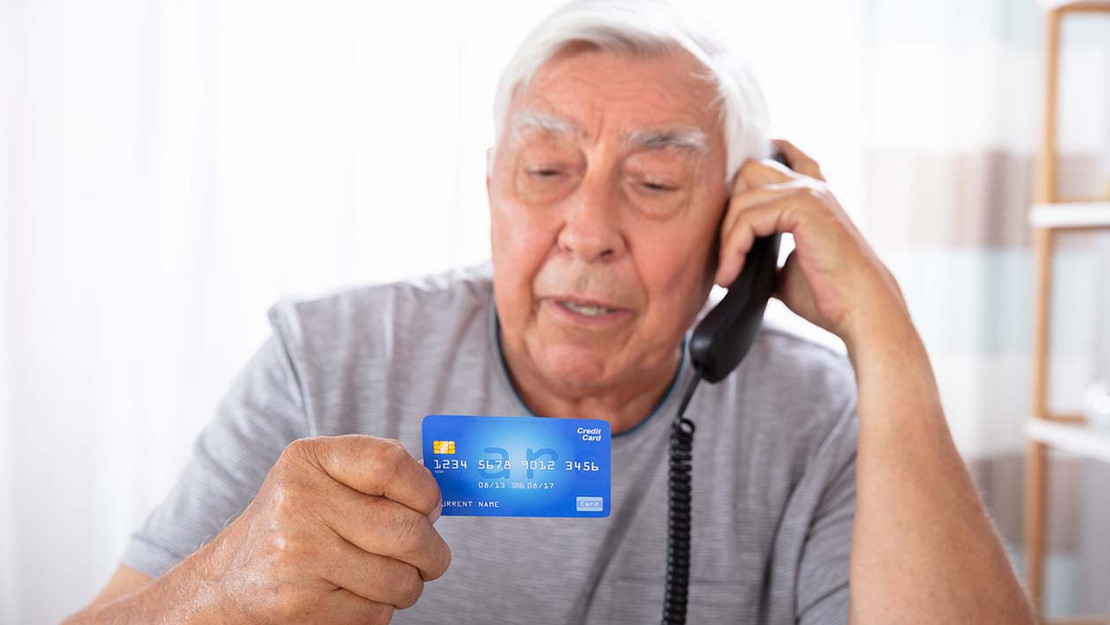 Mann mit Telefonhörer hält seine Kreditkarte in der Hand. 