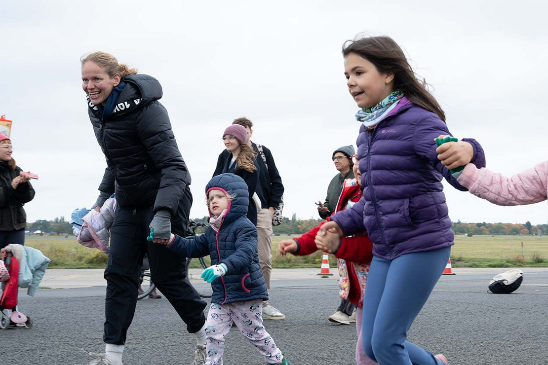 Kinder mit Eltern an den Händen rennen über eine Asphaltstrecke