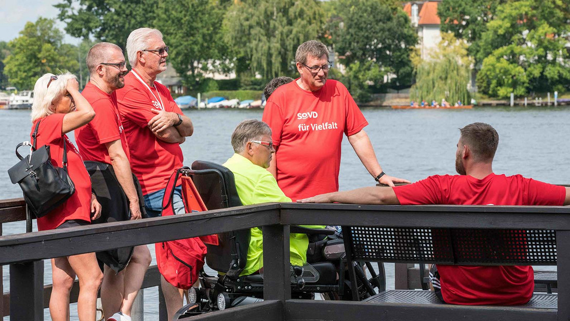 Menschengruppe mit Frau im Rollstuhl Steg. 