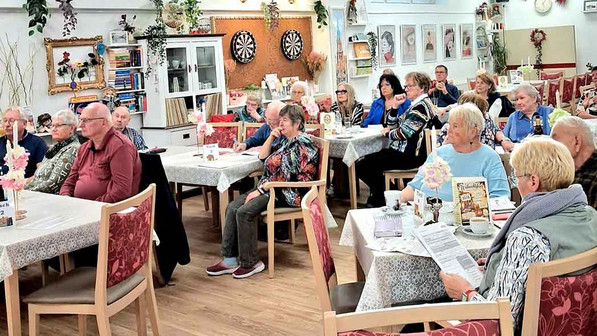 Viele Menschen sitzen an Tischen und hören zu.