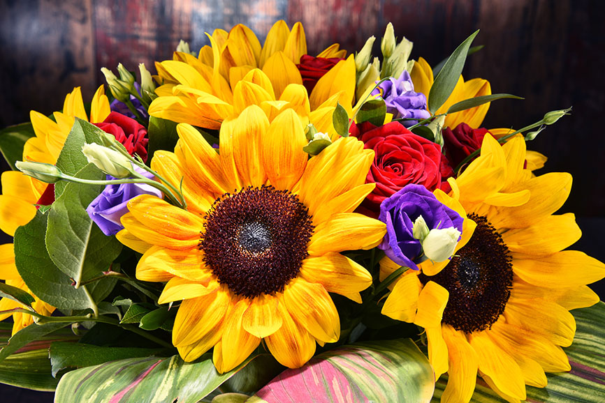 Sommerlicher Blumenstrauß mit Sonnenblumen, roten Rosen und lila Freesien